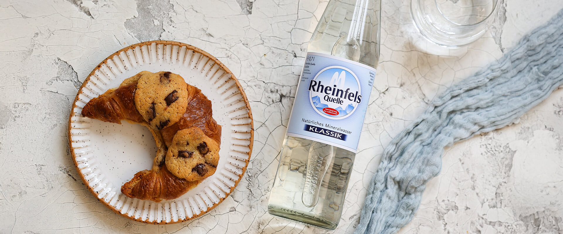 Crookies auf einem Teller liegend. Der Teller steht auf einem Tisch, daneben eine Flasche Rheinfels Quelle Klassik 0,7 L Glas Mehrweg.