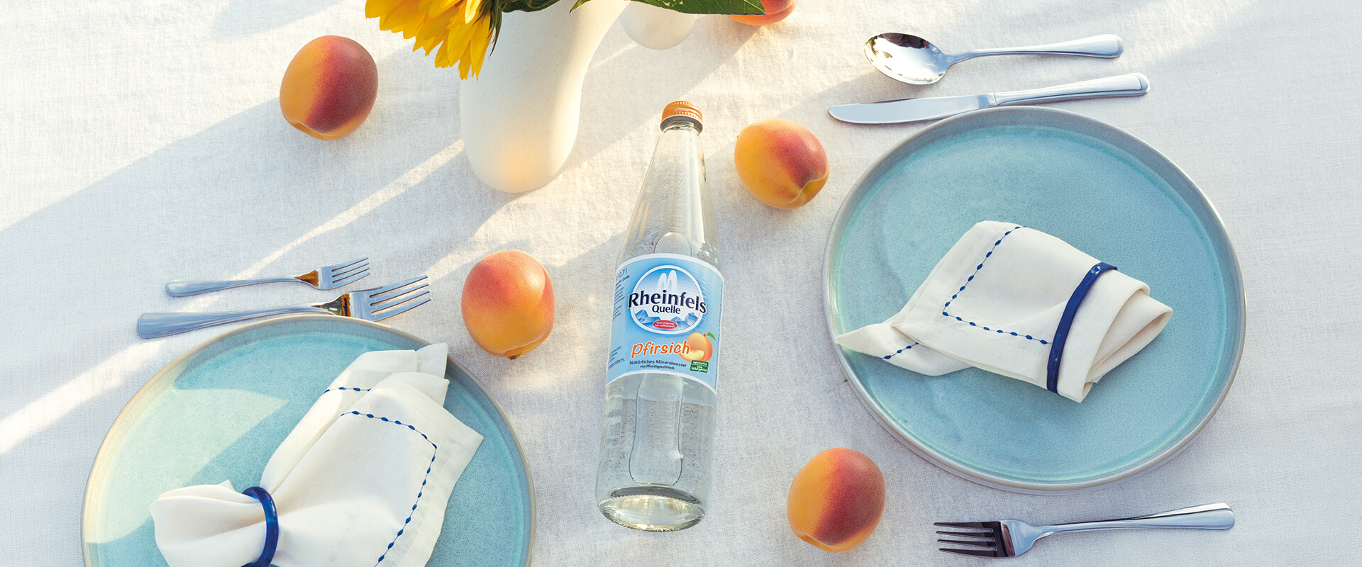 Rheinfels Quelle Pfirsich Glas-Flasche auf einem gedeckten Tisch mit Pfirsich Früchten dekoriert
