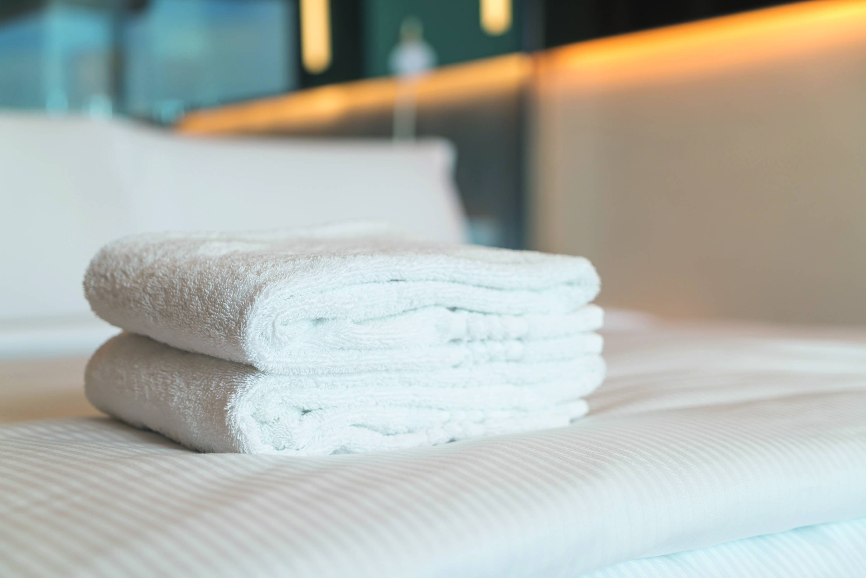 Zwei weiße Handrücher zusammengelegt auf einem Bett